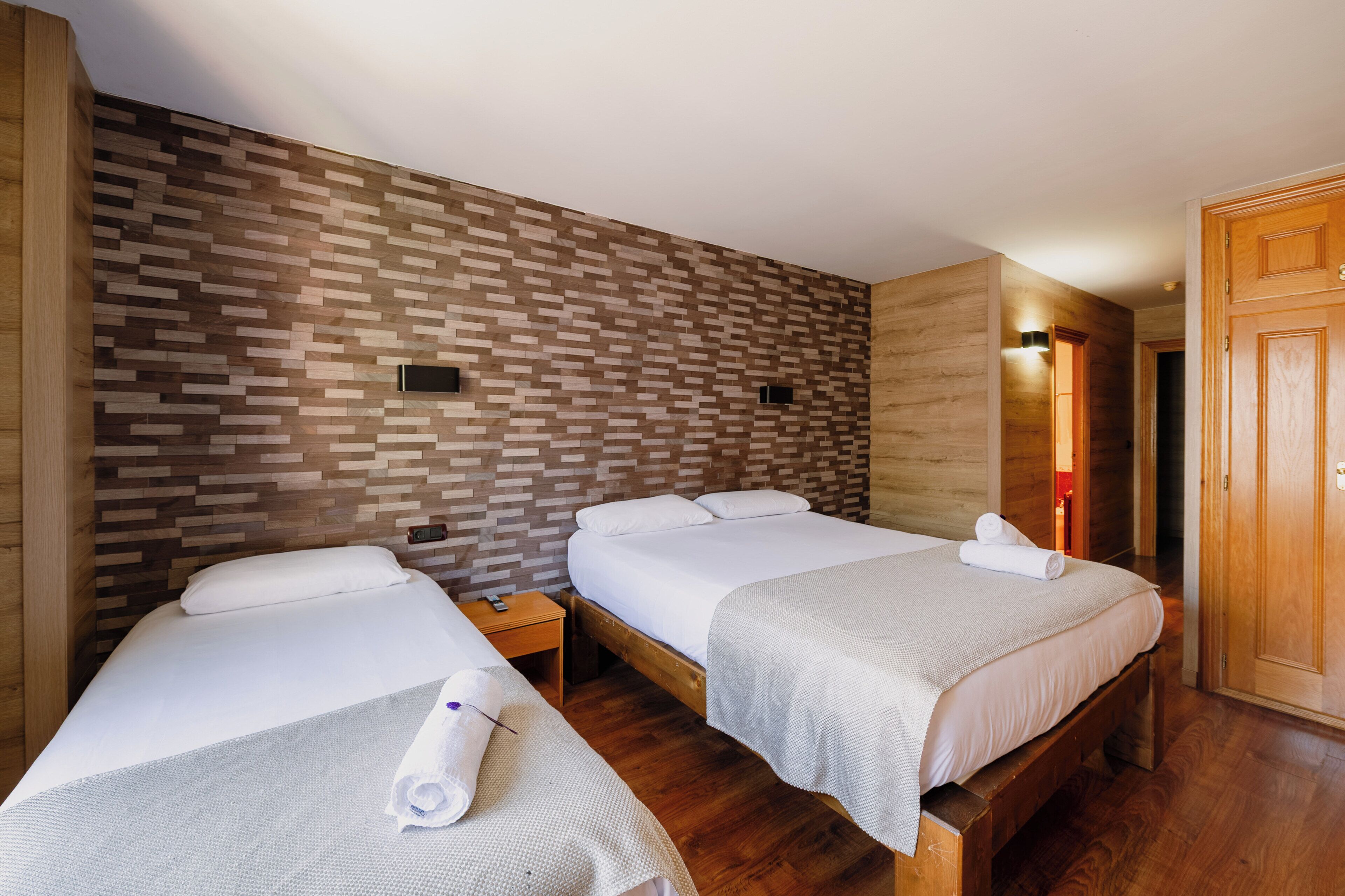 Habitación de hotel con dos camas, suelo de madera, pared con diseño de ladrillo y armario de madera.