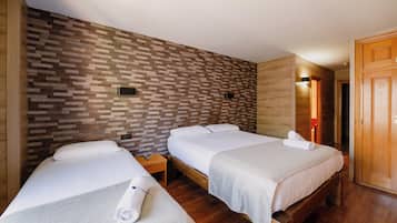 A hotel room with two beds, wooden flooring, a brick-patterned wall, and a wooden wardrobe.