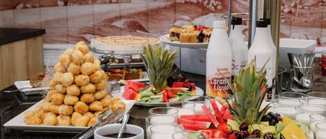 Een buffettafel met diverse gerechten, waaronder een piramide van donuts, fruit en zuivelproducten.
