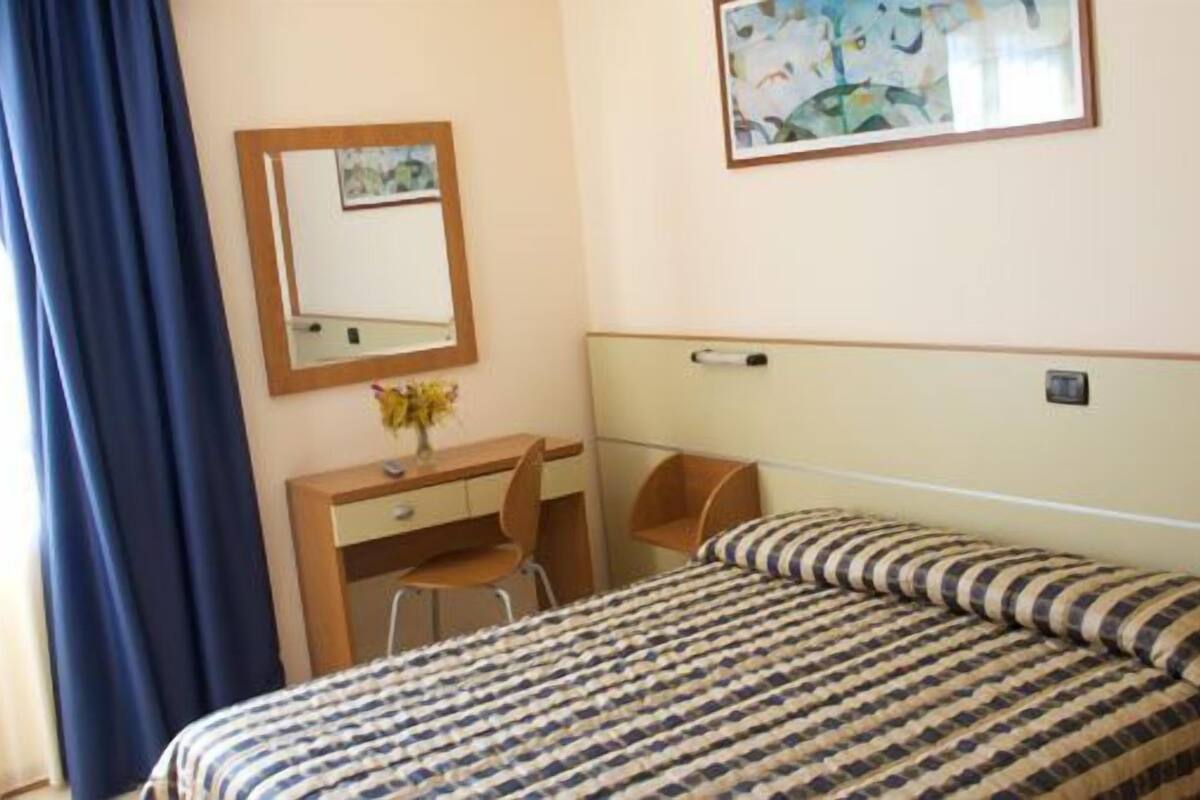 Een hotelkamer met een bed, een bureau, een stoel, een spiegel en een schilderij aan de muur.