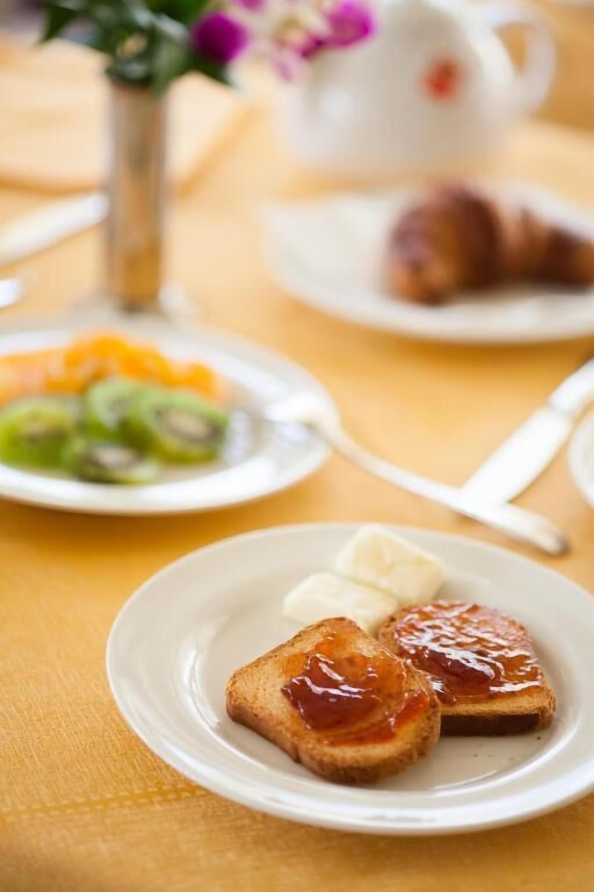 A breakfast setting with toast, butter, jam, and sliced fruit on a plate.