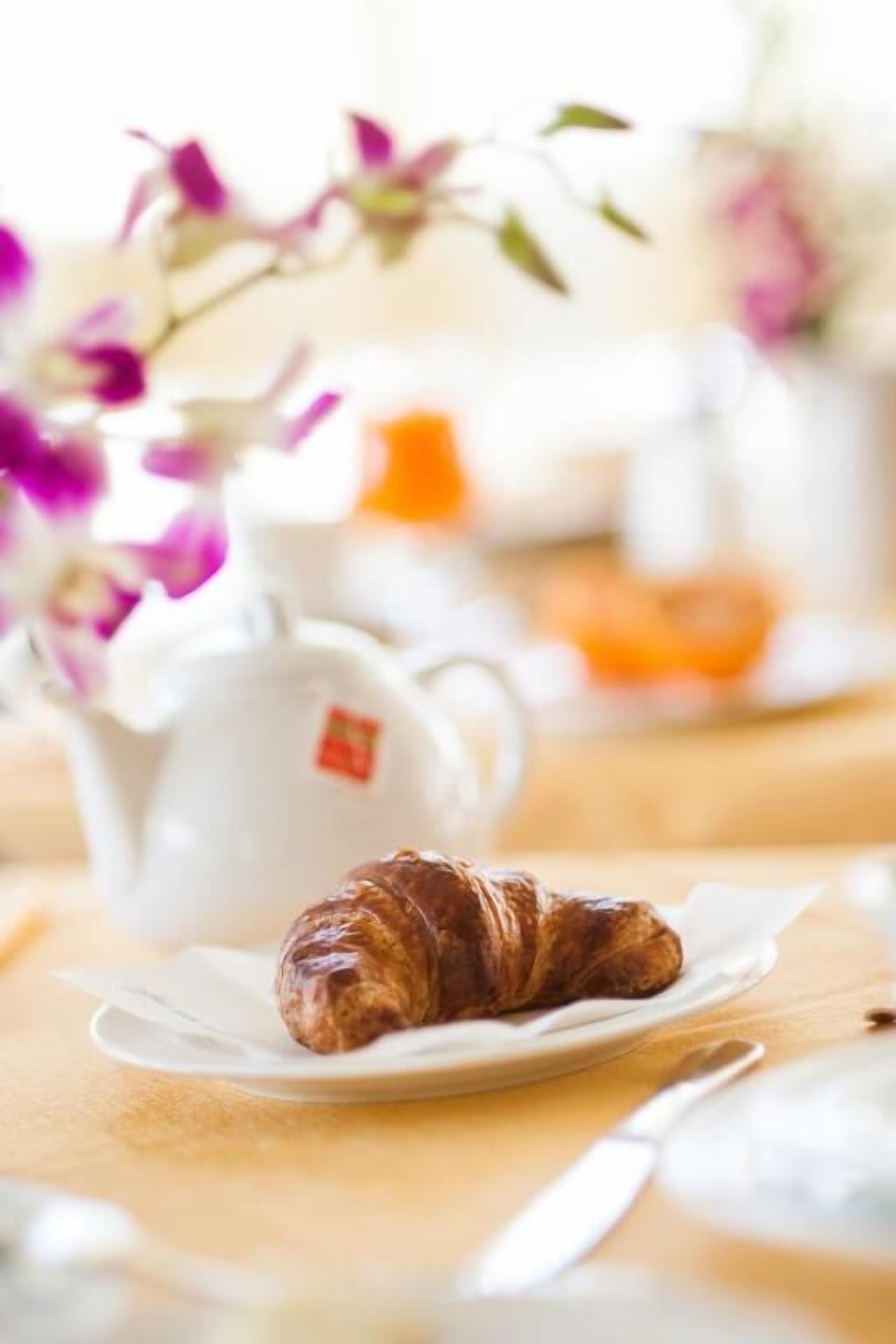 A croissant on a plate with a teapot and a cup in the background.