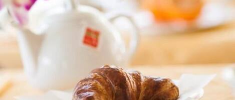 A croissant on a plate with a teapot and a cup in the background.
