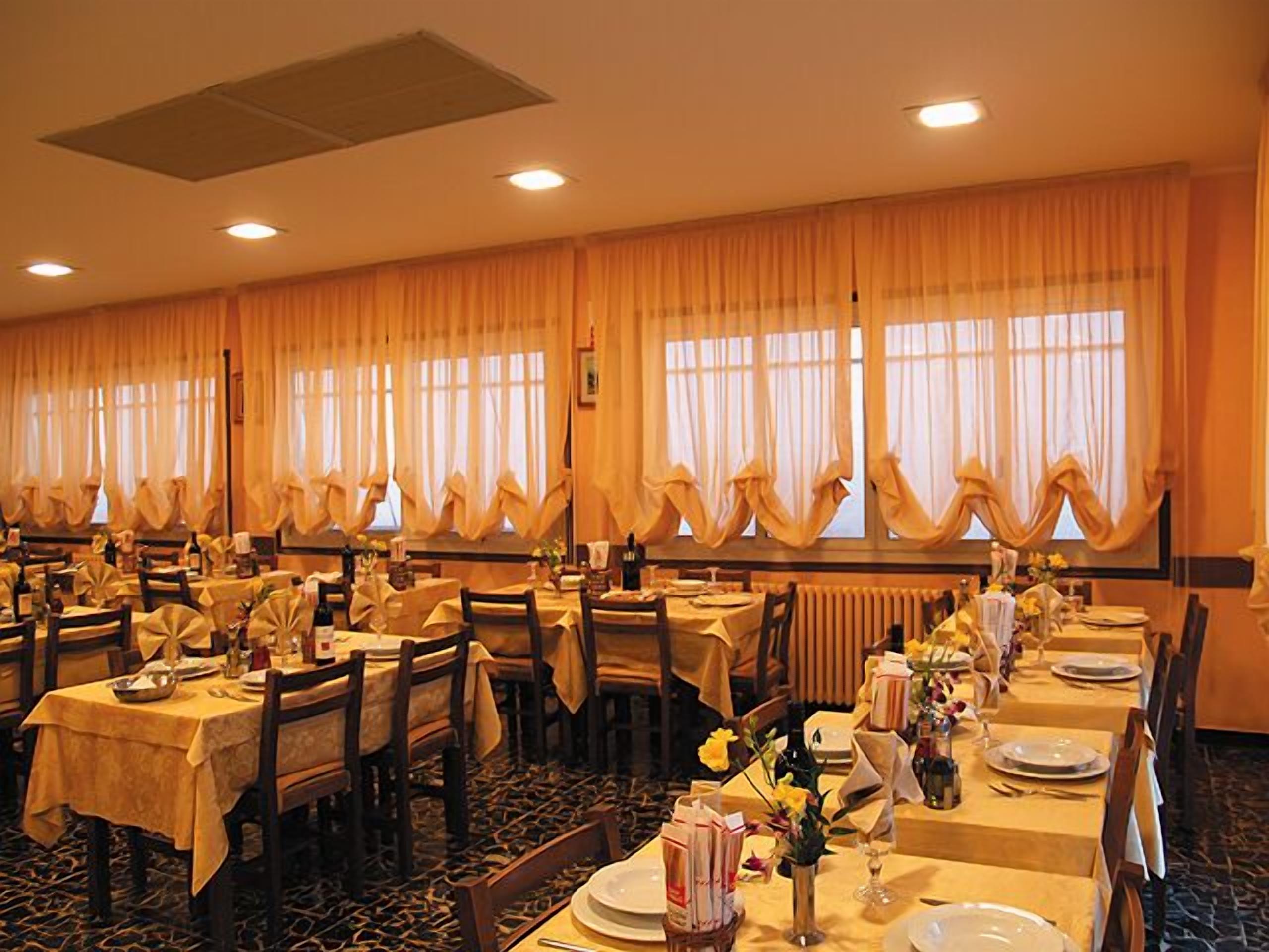 Un salón de banquetes con varias mesas dispuestas para comer, ventanas amplias con cortinas y piso alfombrado.