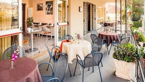 Un área de comedor al aire libre con mesas y sillas, una planta en maceta y vistas de la ciudad.