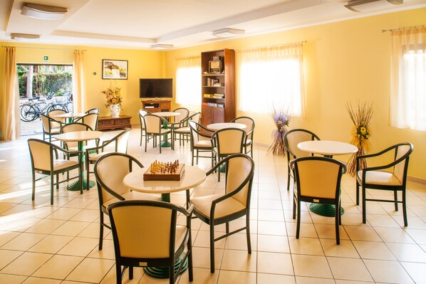 A room with multiple tables and chairs, a television, a bookshelf, and a chessboard. - Hotel Candido (Diano Marina)