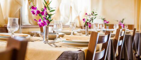 A dining table set with plates, glasses, and cutlery, with chairs and a vase of flowers.
