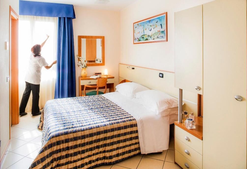 A hotel room with a bed, a desk, a chair, a dresser, and a painting on the wall.