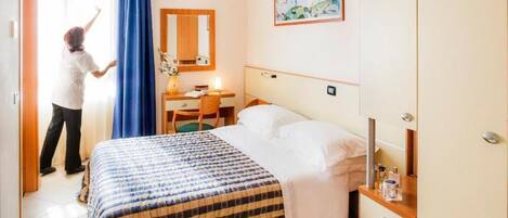 A hotel room with a bed, a desk, a chair, a dresser, and a painting on the wall.