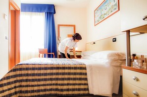 A hotel room with a bed, a bedside table, a chair, and a window with blue curtains. - Hotel Candido (Diano Marina)