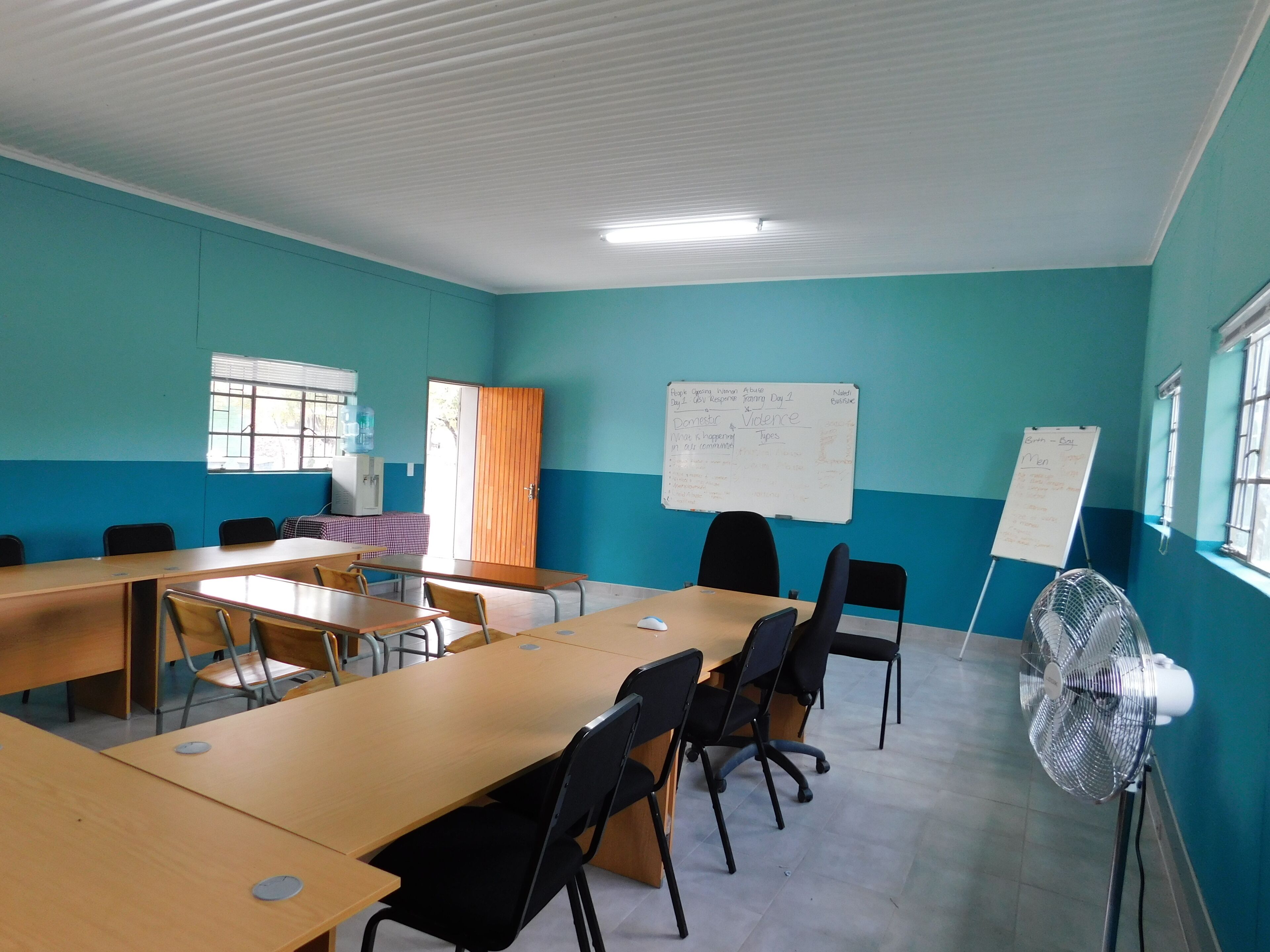 A conference room with teal walls, a whiteboard, and a fan.
