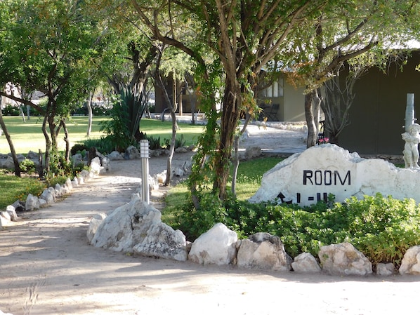 A pathway leading to a building with a 'ROOM' sign, surrounded by rocks and greenery.