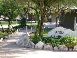 A pathway leading to a building with a 'ROOM' sign, surrounded by rocks and greenery.