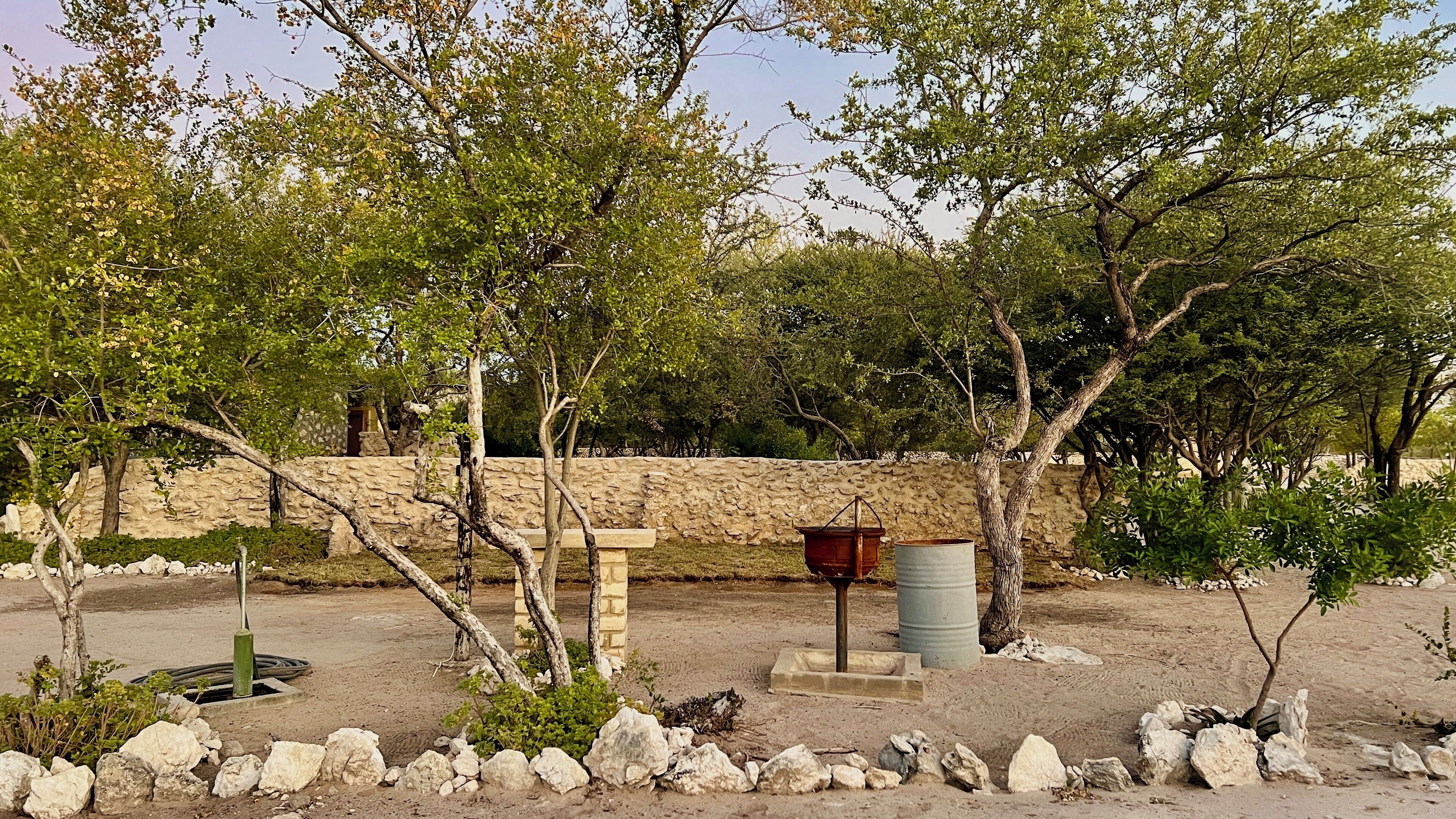 Un espacio rústico al aire libre con un muro de piedra, un banco de madera y un recipiente de metal.