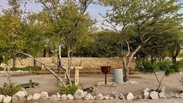Un espacio rústico al aire libre con un muro de piedra, un banco de madera y un recipiente de metal.