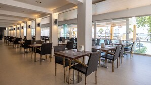 A spacious indoor dining area with multiple tables and chairs, large windows offering views of the outside, and a modern architectural design. - Petunya Beach Resort - All Inclusive (Bodrum)