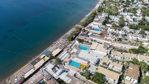 An aerial view of a coastal area with a beach, a swimming pool, and residential buildings. - Petunya Beach Resort - All Inclusive (Bodrum)