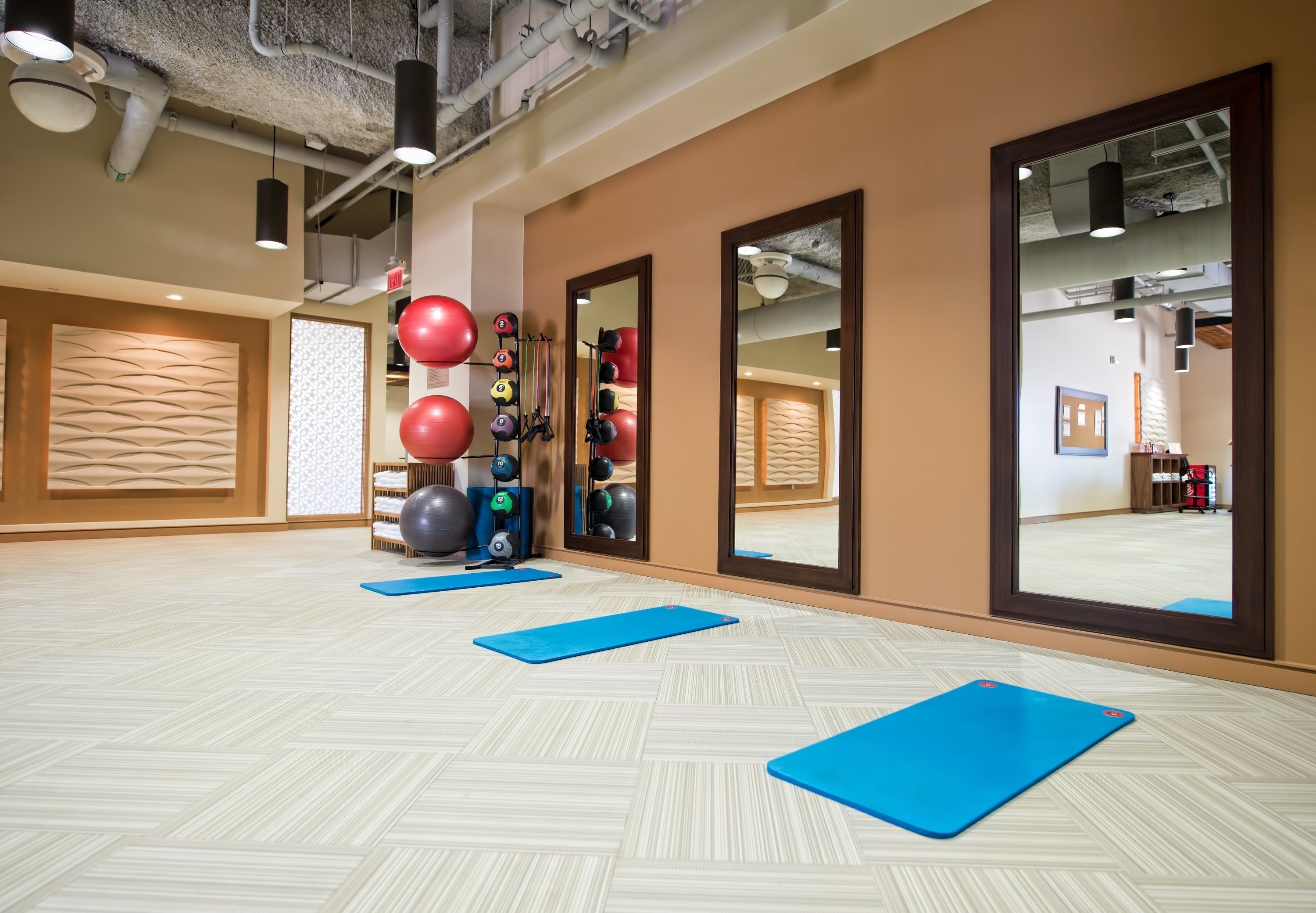 A gym with exercise equipment, blue mats, and large mirrors.