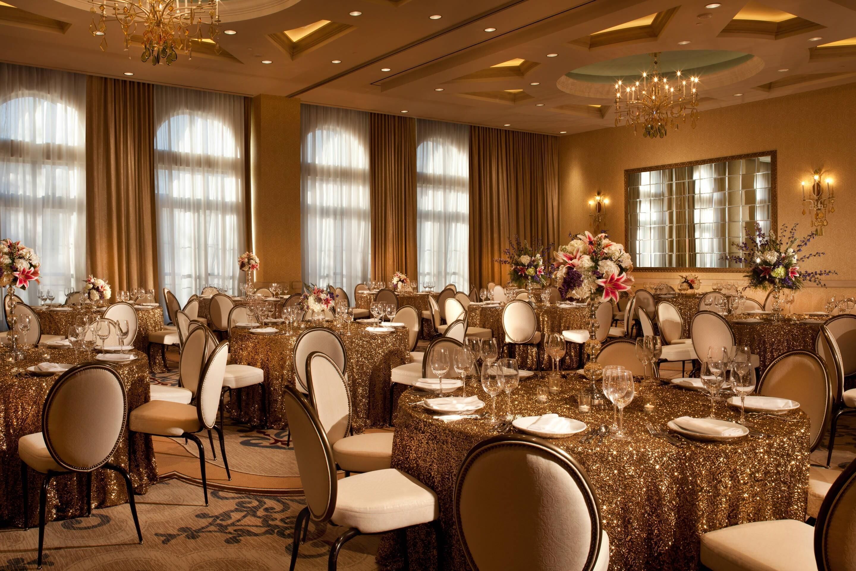 A banquet hall with round tables covered in gold tablecloths, arranged in rows with chairs.