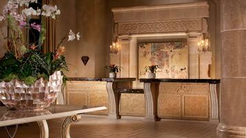 A lobby with a marble reception desk, a large decorative plant, a fireplace with a mosaic, and a wall-mounted light fixture.