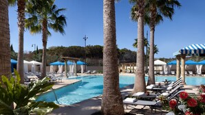 A pool area with lounge chairs, palm trees, and umbrellas.