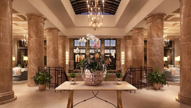 A spacious lobby with marble columns, a central table with a decorative vase, and a chandelier.