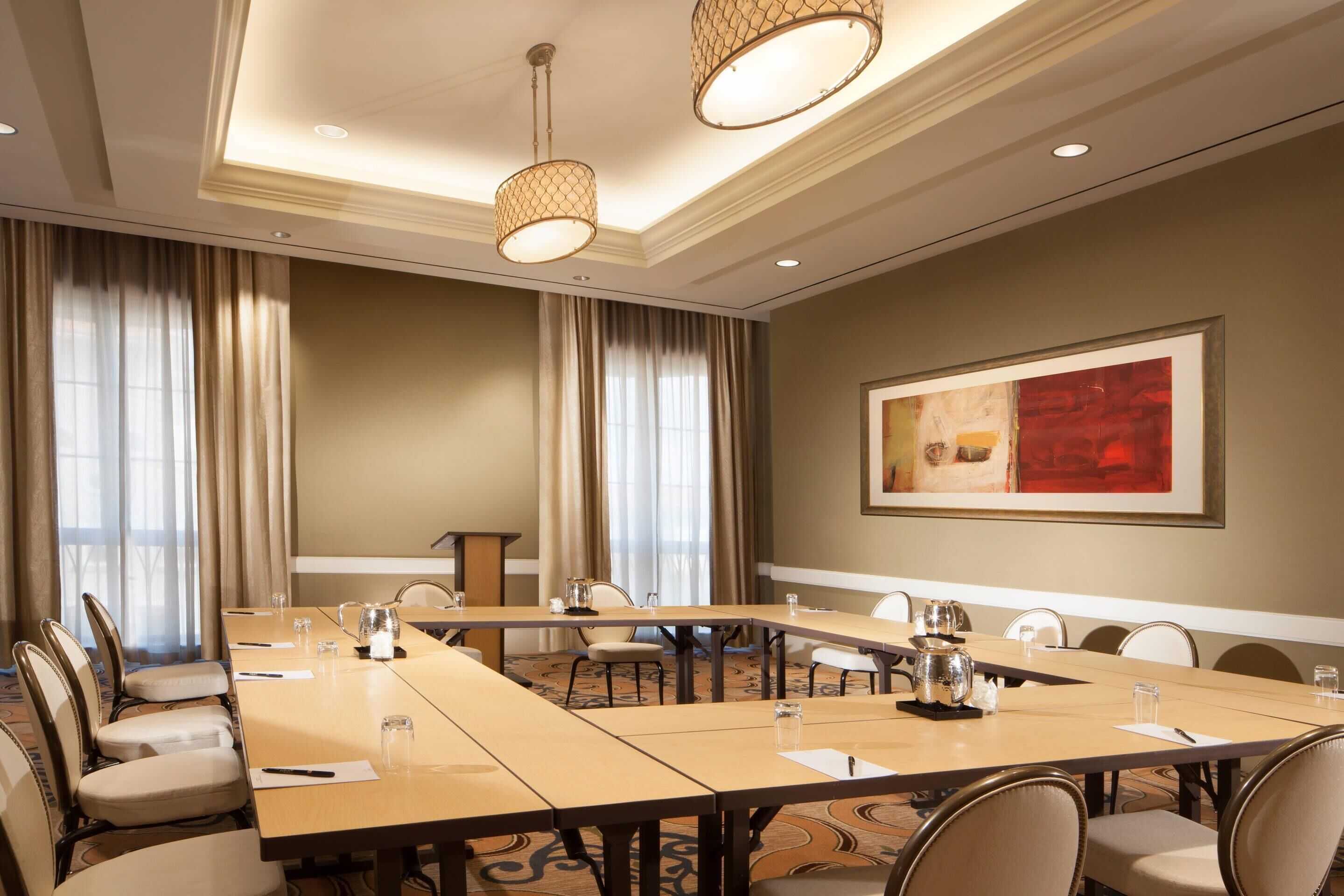 A conference room with a long table, chairs, a projector screen, and a painting on the wall.