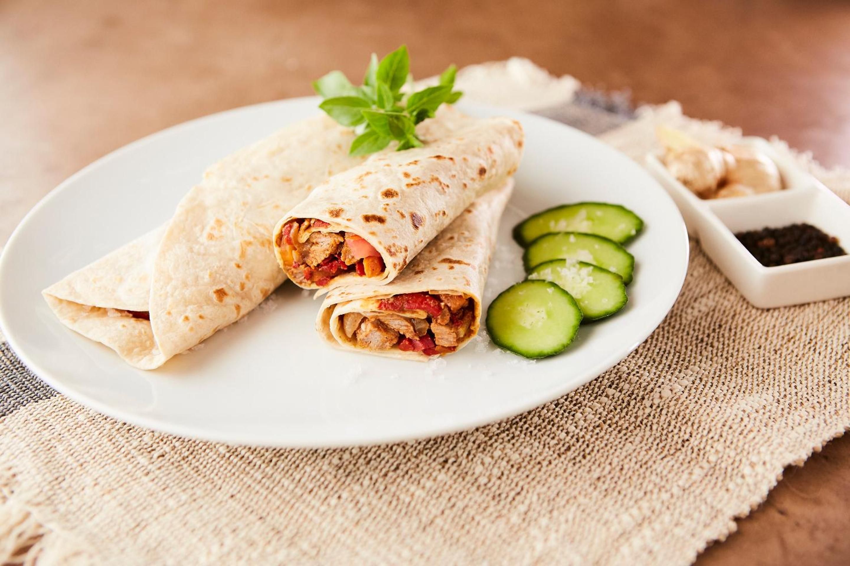 A plate with two rolled wraps, sliced cucumbers, and a small dish of spices.