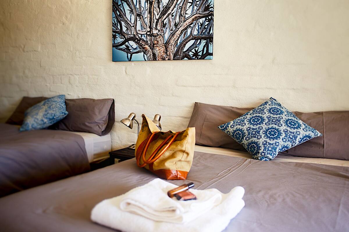 A hotel room with two beds, a large painting on the wall, and a bag on the floor.