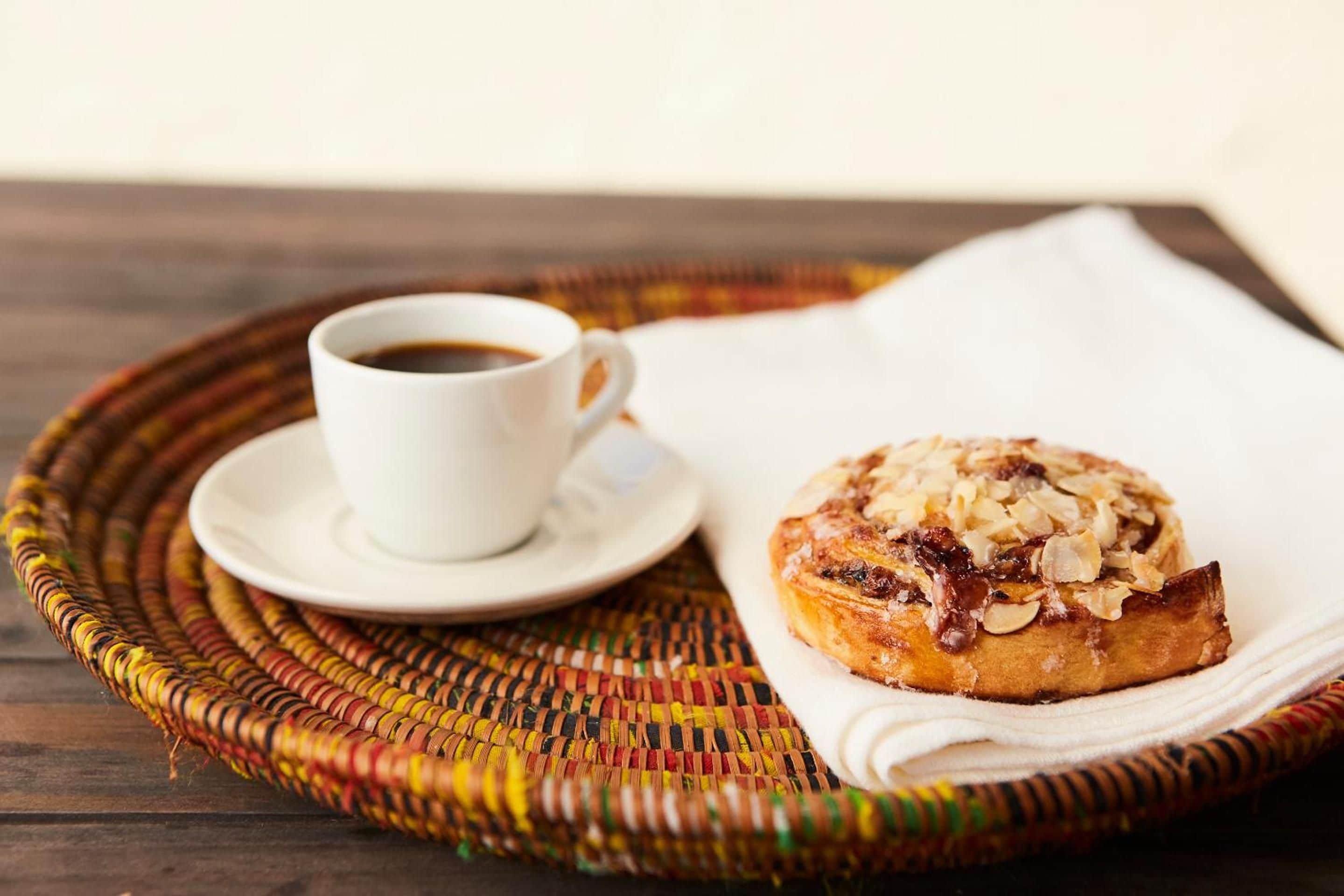 Una tazza di caffè su un vassoio di vimini con un pasticcino su un tovagliolo.