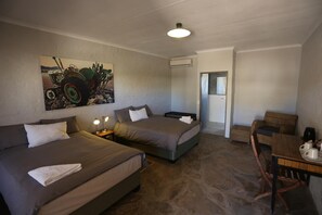 A hotel room with two beds, a painting, a desk with chairs, and an air conditioning unit.