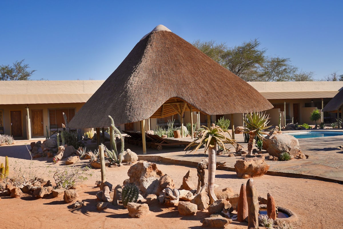 A resort with a thatched-roof structure, desert landscaping, and a pool.