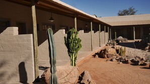 A desert-style building with a covered patio area, large rocks, and cacti. - Solitaire Lodge (Solitaire)
