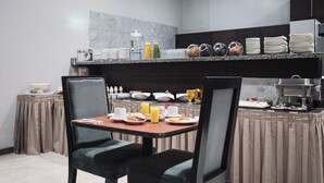 Una disposición para el desayuno con una mesa, sillas y un mostrador de buffet con comida y bebidas.