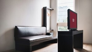 Una habitación moderna con un sofá negro, una mesita y un televisor sobre un mueble.