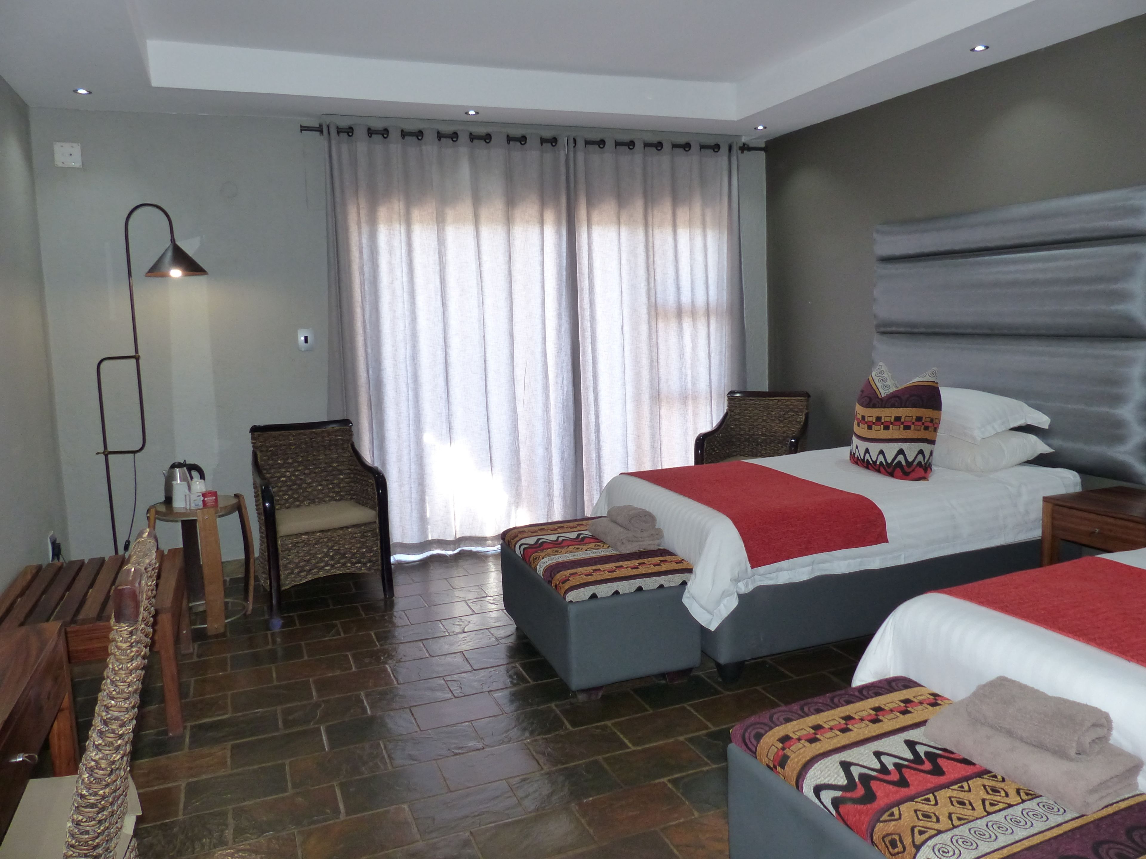 A hotel room with two beds, a chair, a small table, and a lamp.