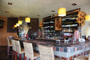 A bar area with a stone counter, wicker chairs, and a variety of bottles.