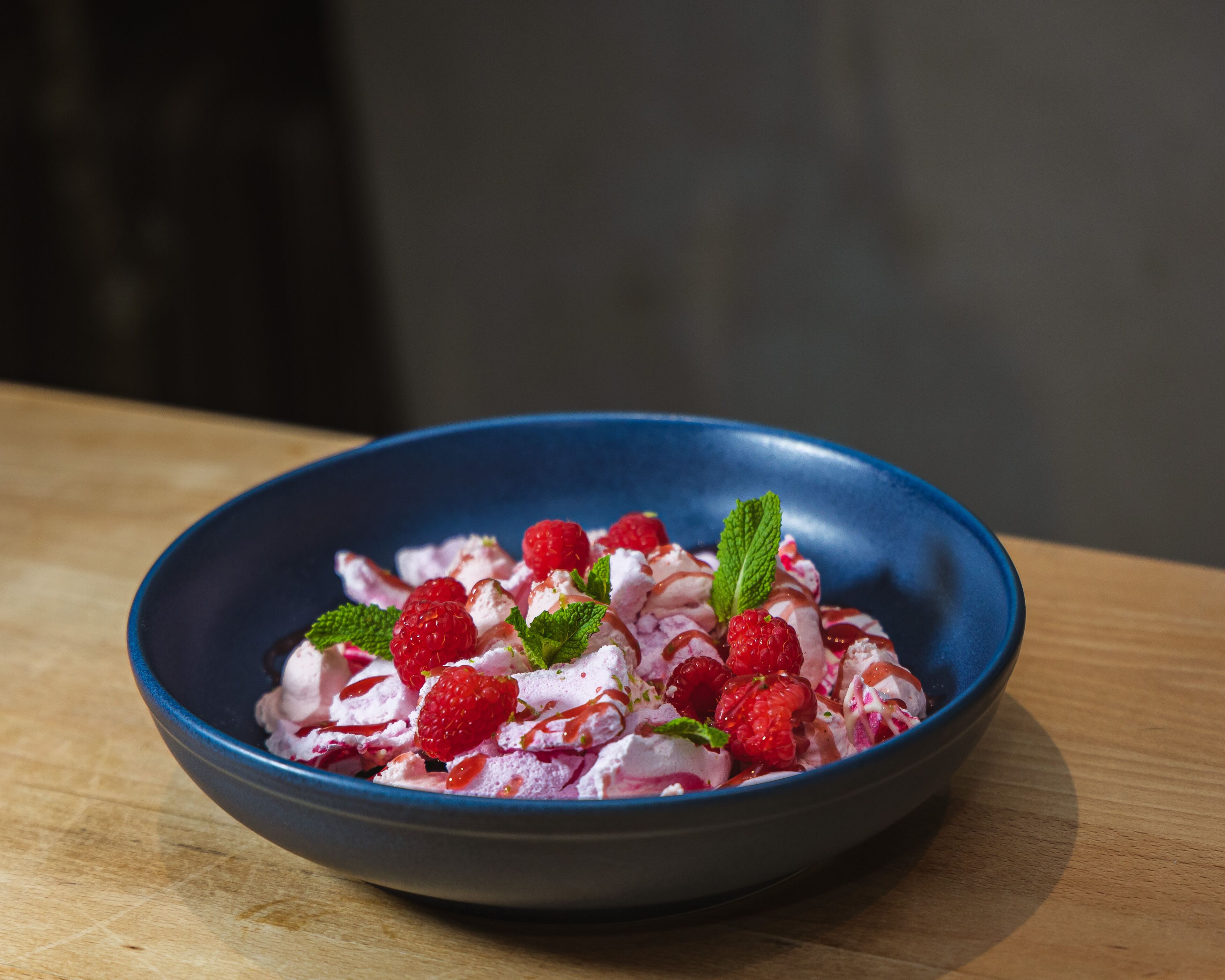 A bowl of dessert with raspberries and mint on a wooden table.