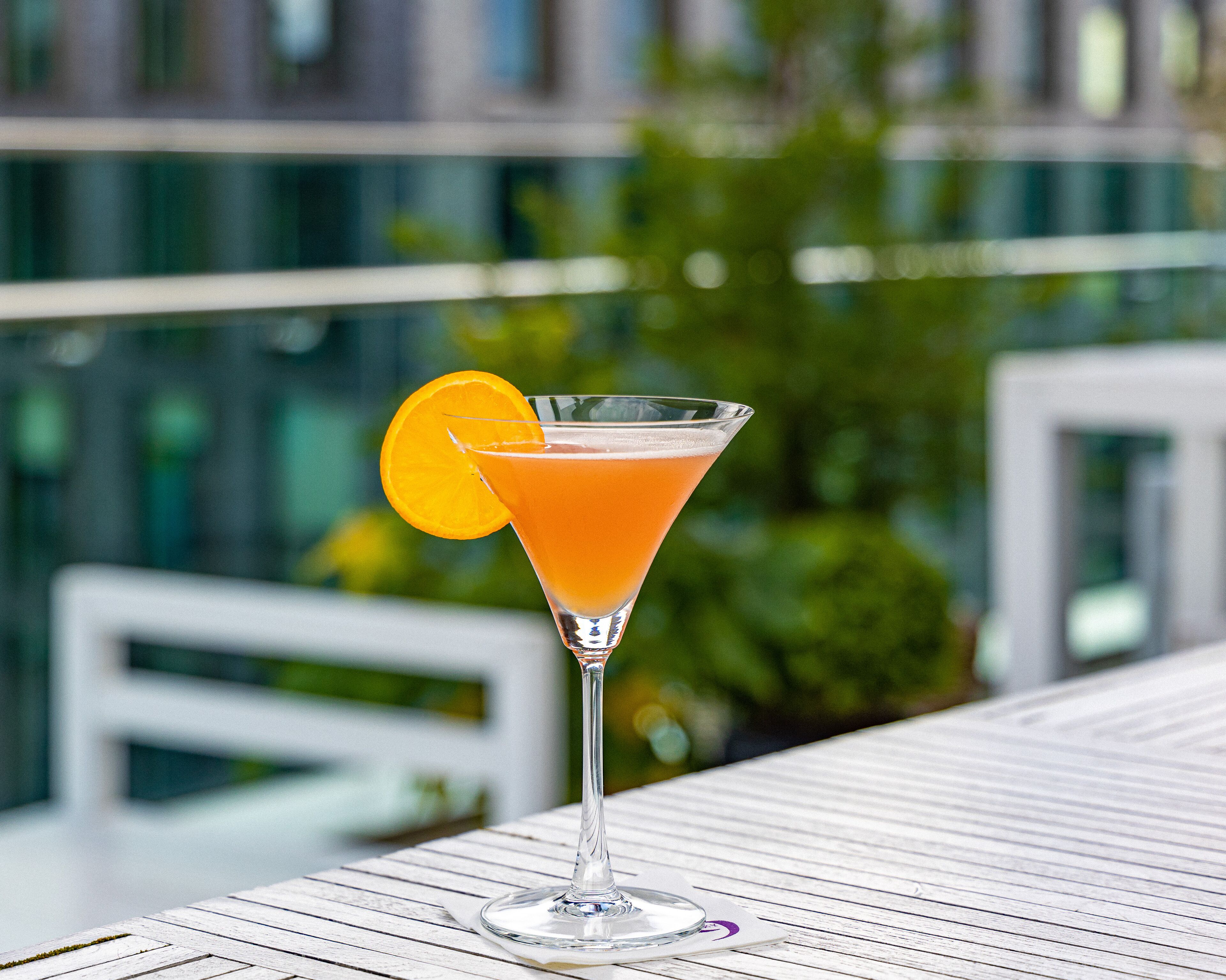 Egy narancsszelettel díszített martini pohár egy fehér, fából készült asztalon.