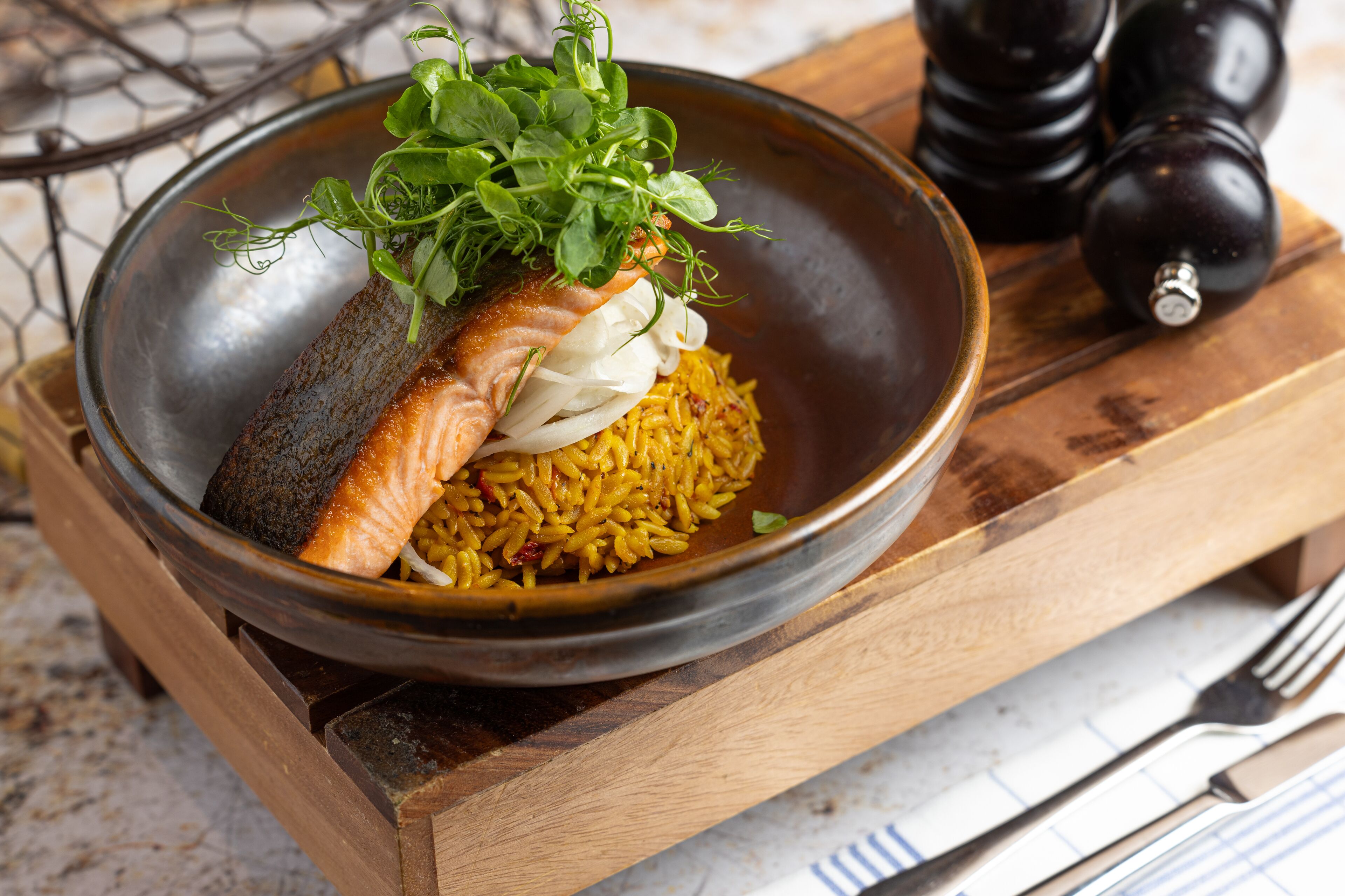 A bowl of food with salmon and rice, garnished with greens, on a wooden board.