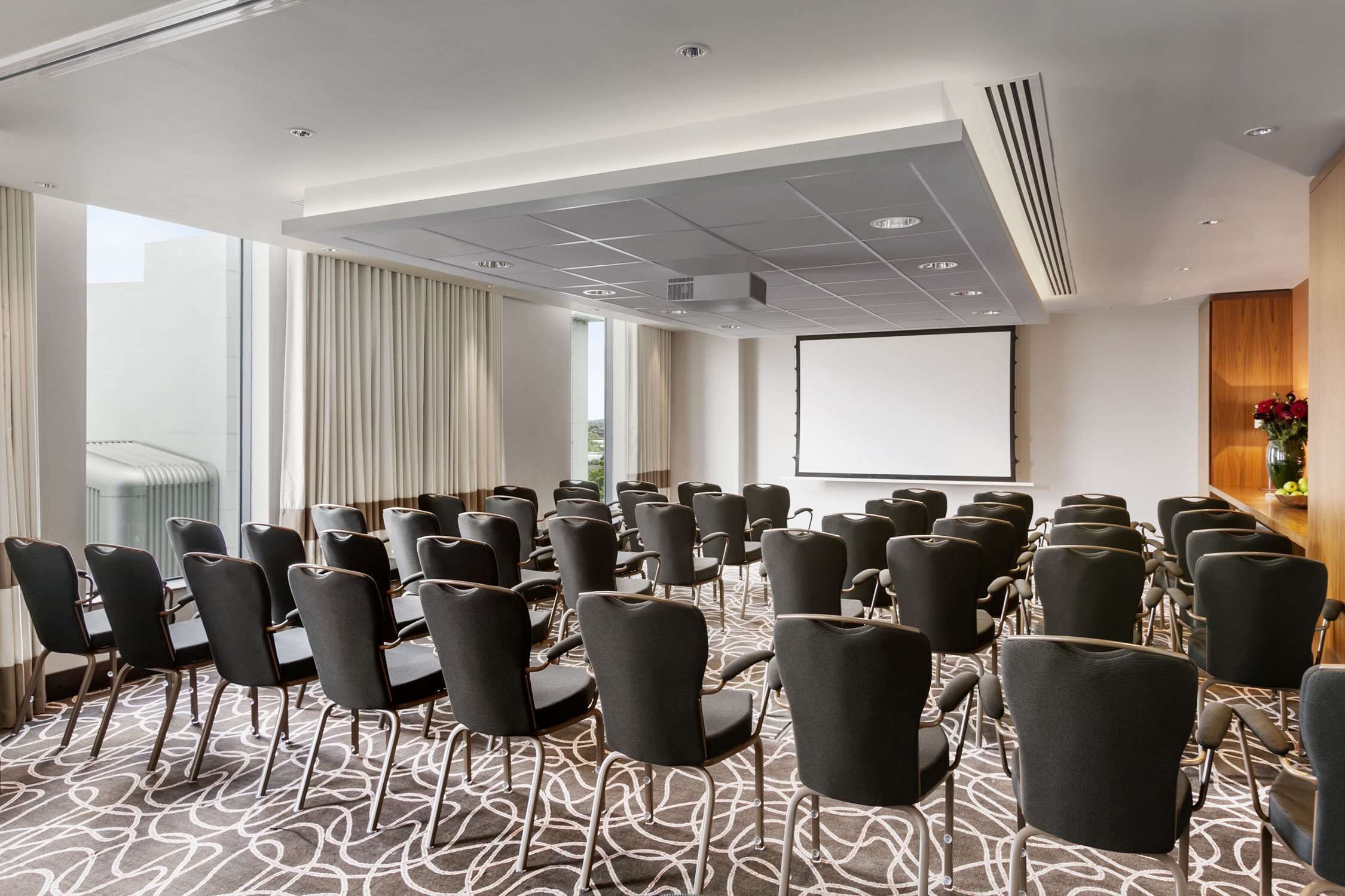 A conference room with rows of chairs, a projector screen, and a large window with curtains.