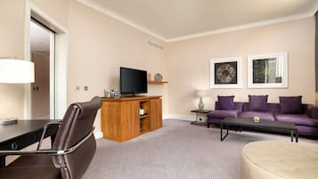 Un salon moderne avec un fauteuil en cuir marron, un meuble de rangement en bois abritant un téléviseur à écran plat, un canapé violet et deux œuvres d’art encadrées accrochées au mur.