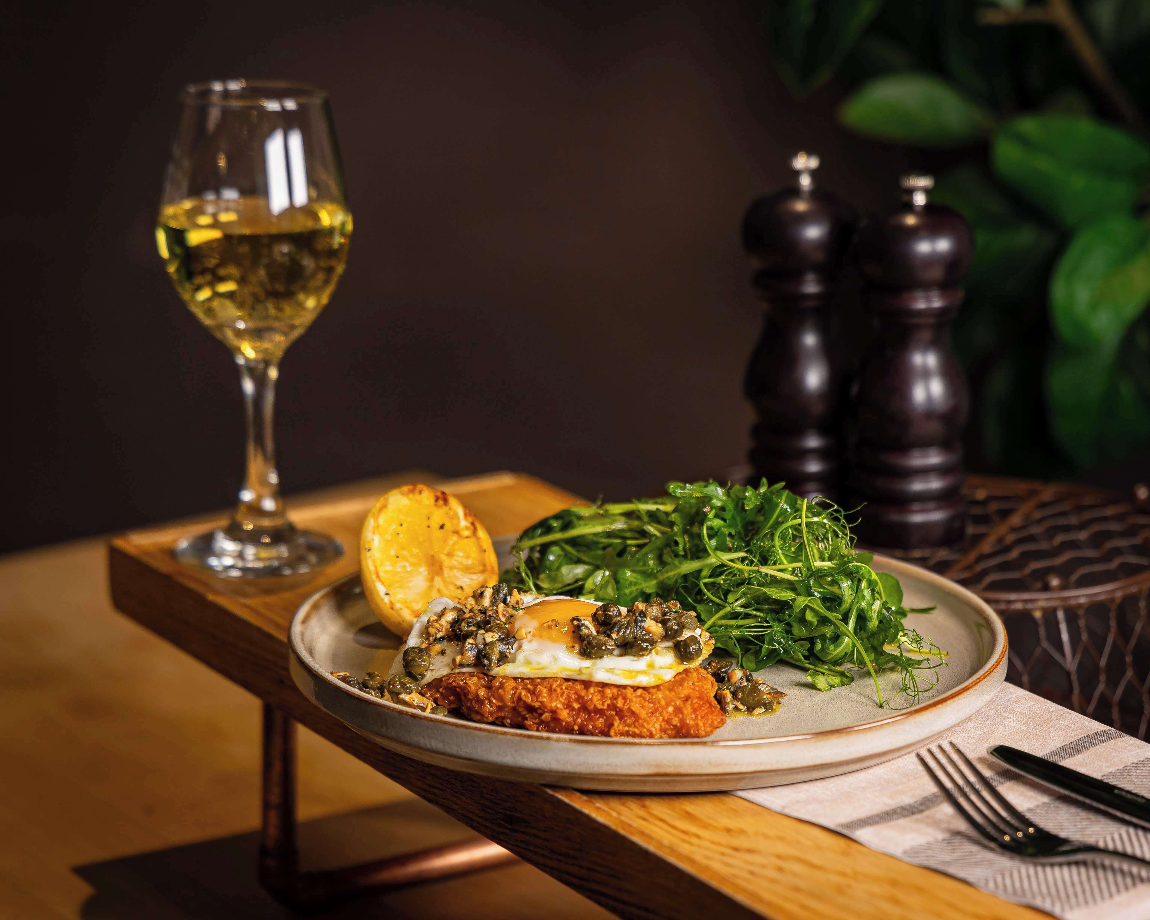 A plate with a fried egg, greens, and a slice of lemon on a wooden table.