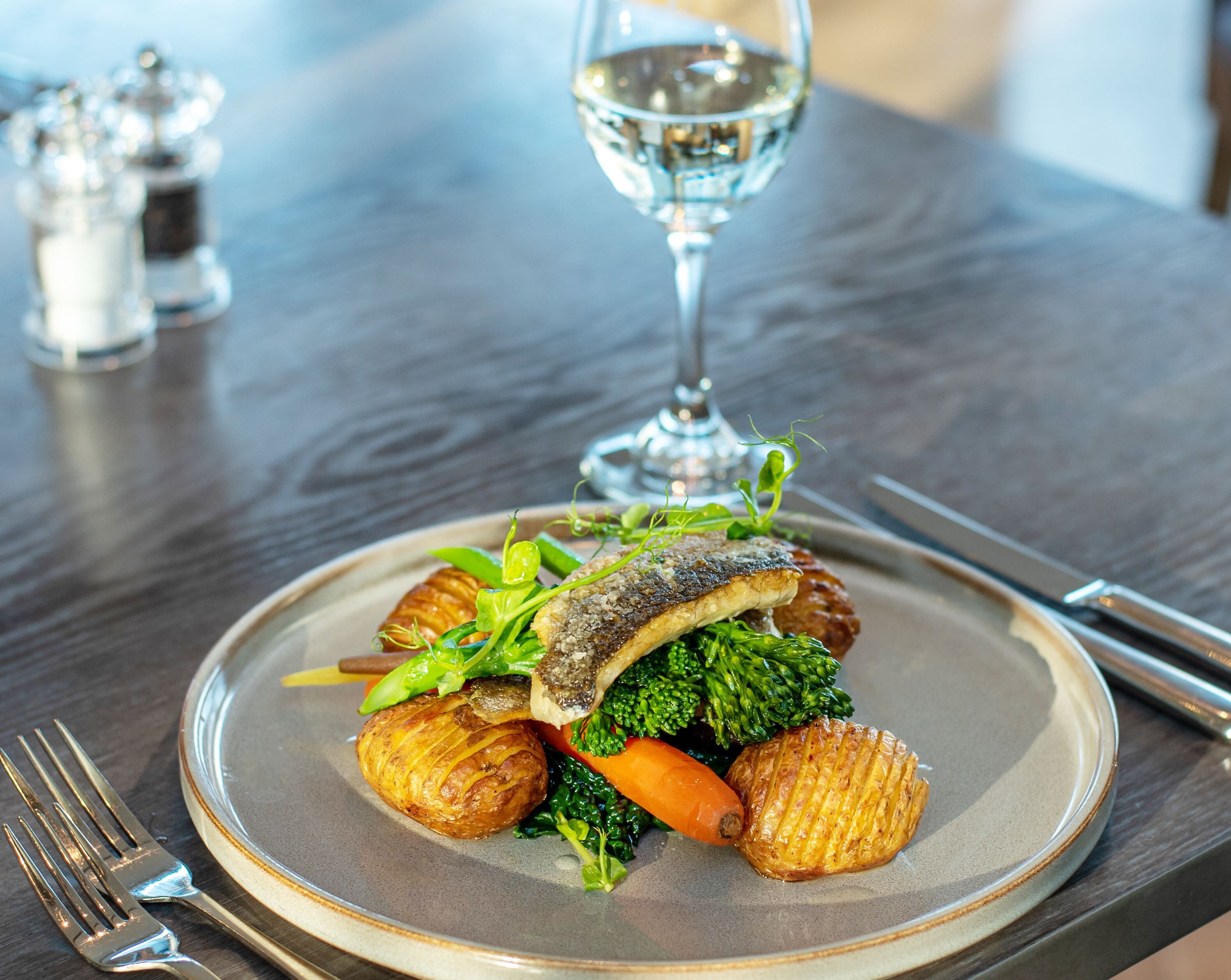 A plate of food with a glass of white wine on a table.