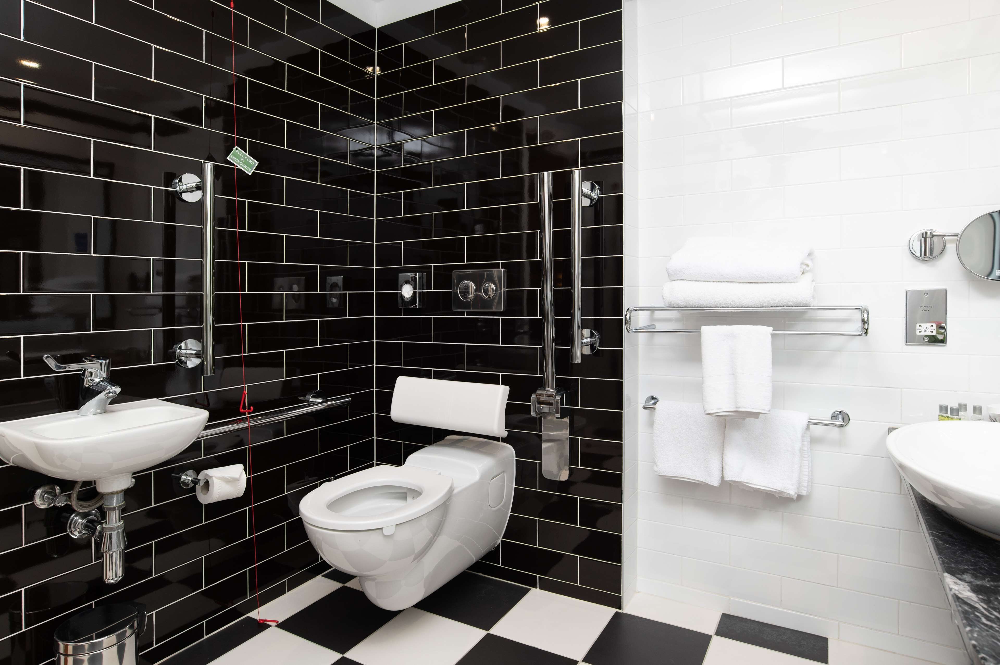 A modern bathroom with black and white tiled walls, a white sink, a toilet, and a shower area.