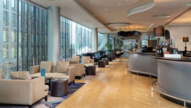 Un'ampia hall con arredi moderni, un'area bar e grandi finestre che offrono vista sulla città.