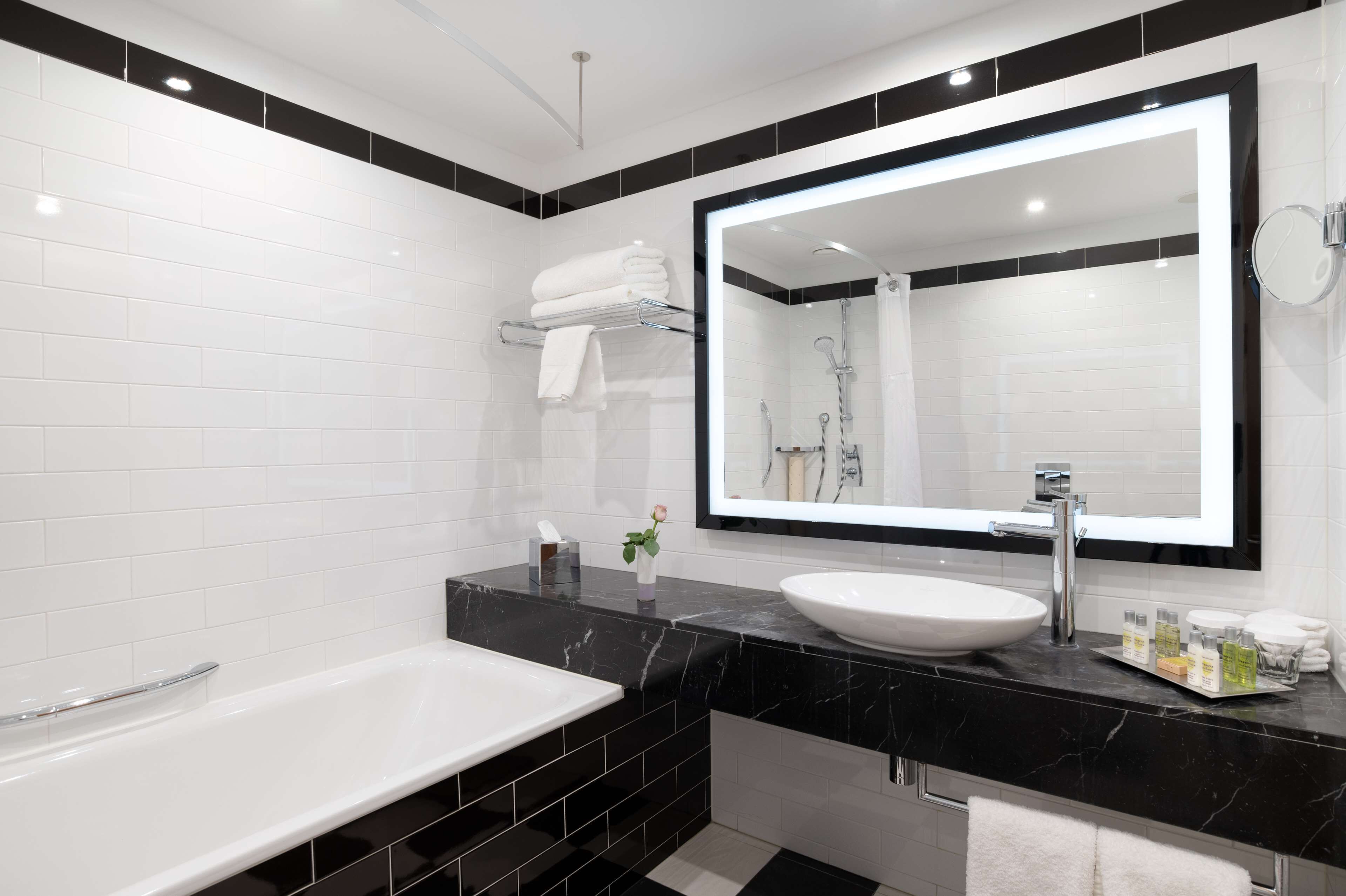 A modern bathroom with a white bathtub, a large mirror, and a black marble countertop.