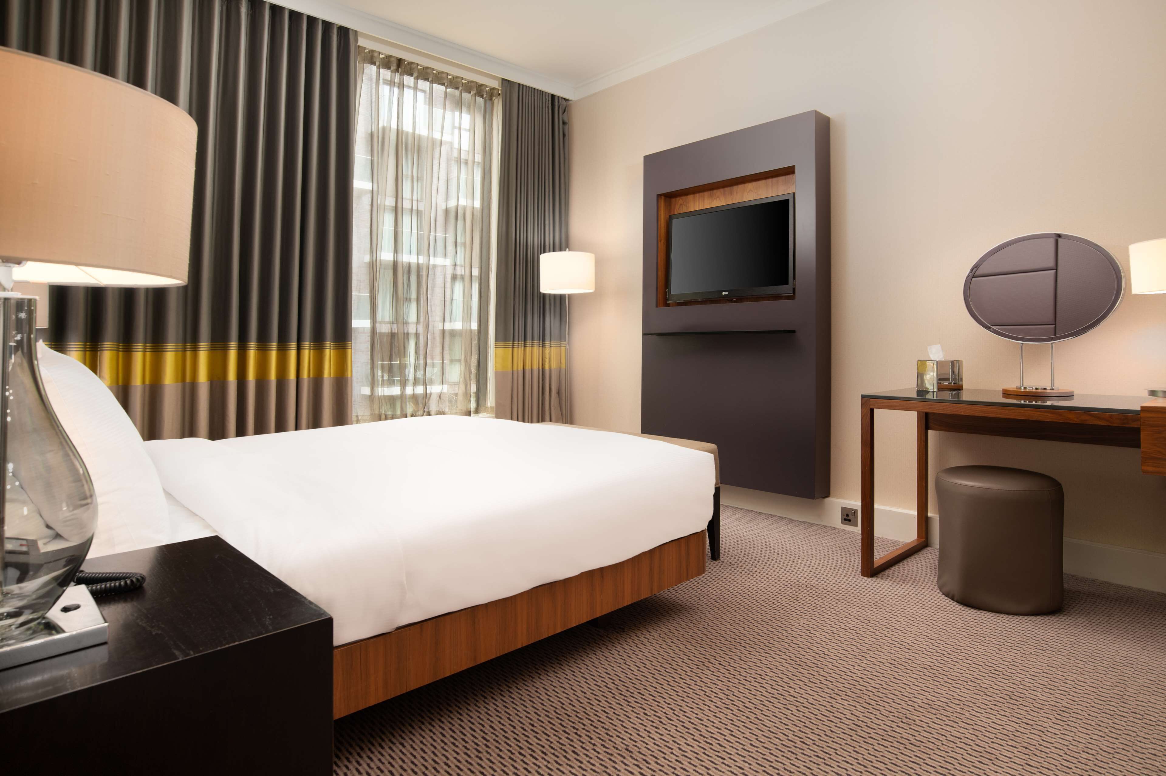A hotel room with a large bed, a desk, a television, and a lamp.