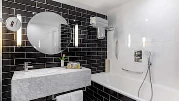A modern bathroom with a white bathtub, a round mirror, a white sink, and black tiled walls.