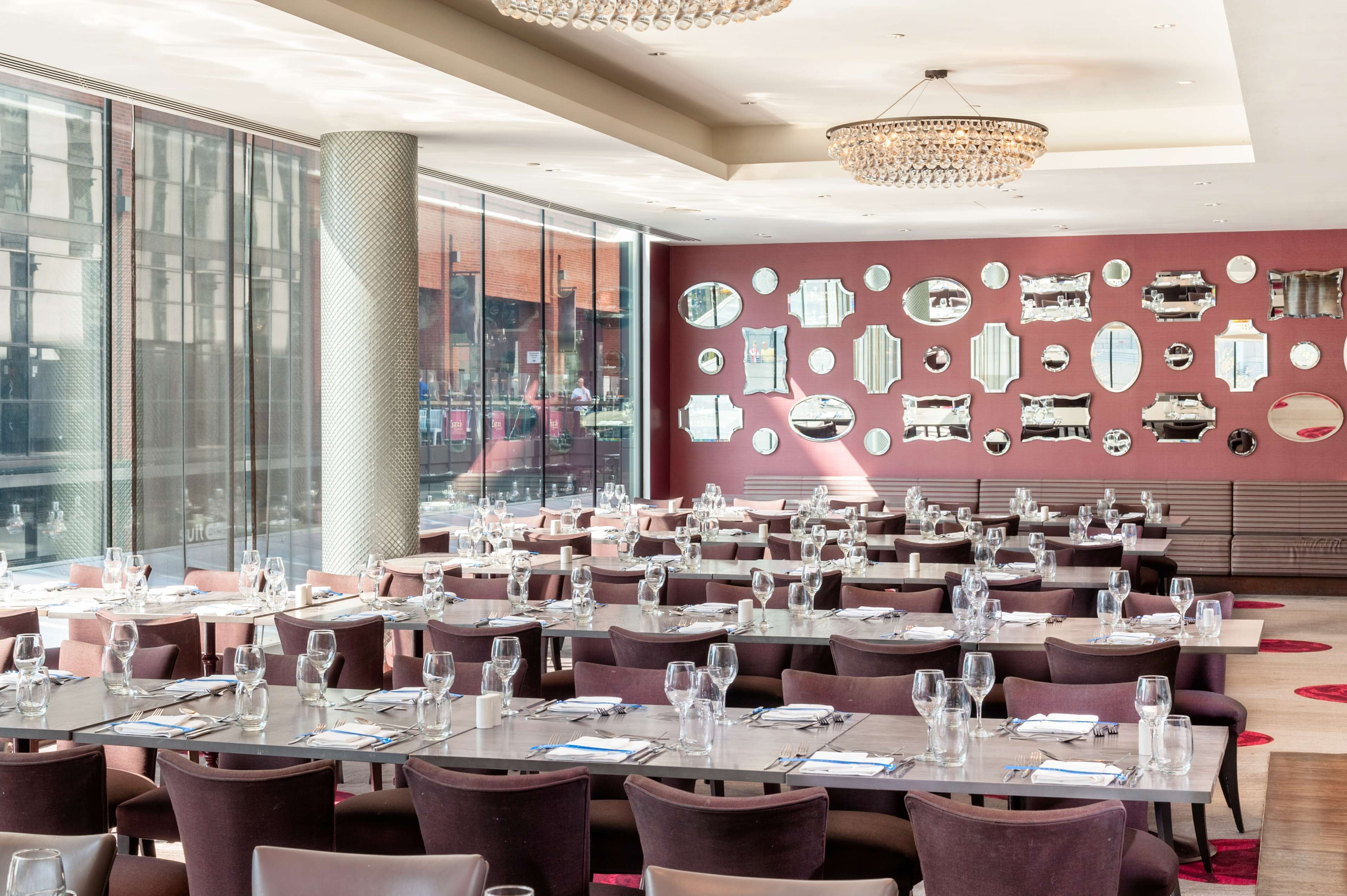 A spacious dining area with tables set for guests, large windows, and a wall decorated with mirrors.